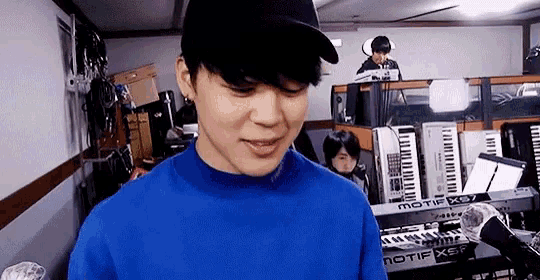 a man wearing a blue sweater and a hat is standing in front of a keyboard .