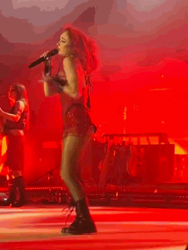 a woman is singing into a microphone on a stage in a red dress .