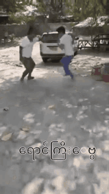 two men are dancing in front of a car with foreign writing on it
