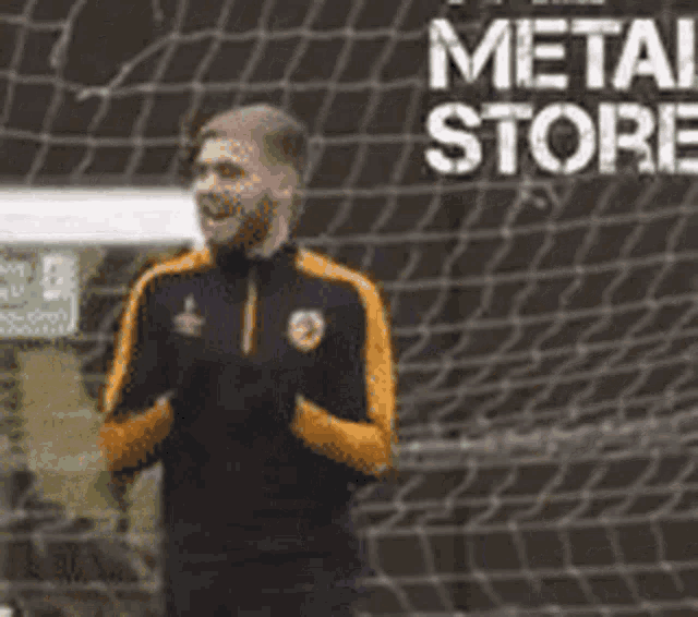 a man is standing in front of a soccer net with the words metal store written on it .