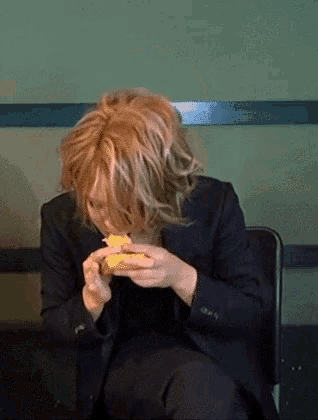 a woman in a black suit is sitting in a chair eating a sandwich