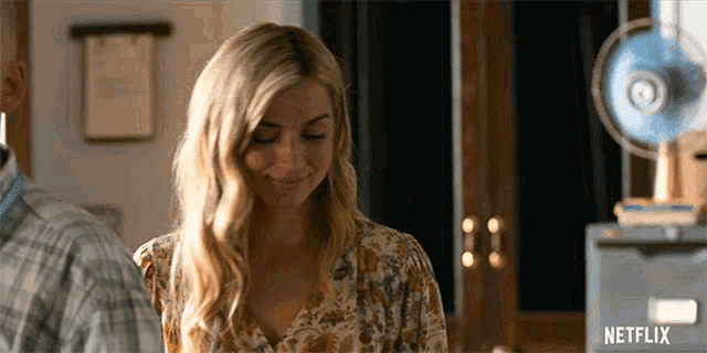 a woman in a floral shirt is smiling in front of a netflix sign