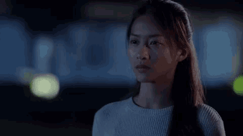 a woman in a white sweater is standing in the dark looking at something .