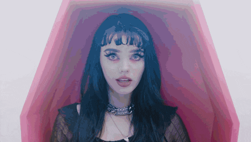 a woman with black hair and red eyes is in a pink coffin .