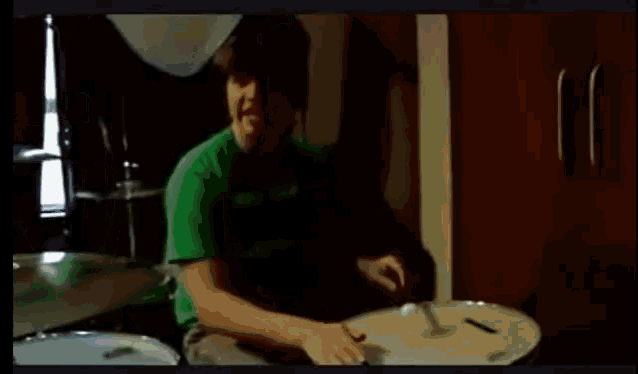 a man in a green shirt is playing drums in a dark room