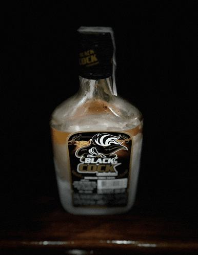 a bottle of black cock sits on a wooden shelf