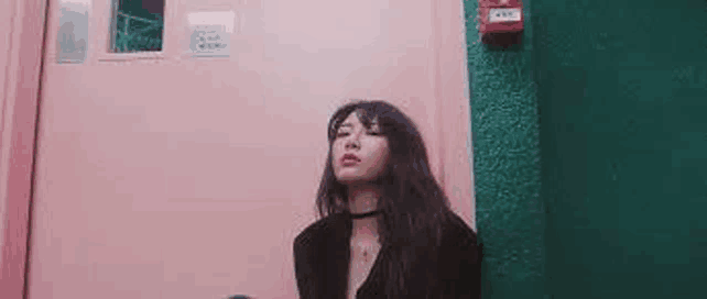 a woman is standing in front of a pink door and a green wall .