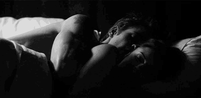 a black and white photo of a man and a woman sleeping in bed .