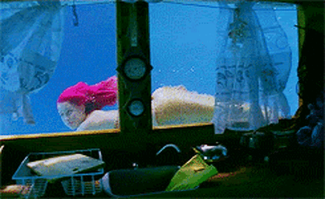 a woman with pink hair is swimming underwater in a tank