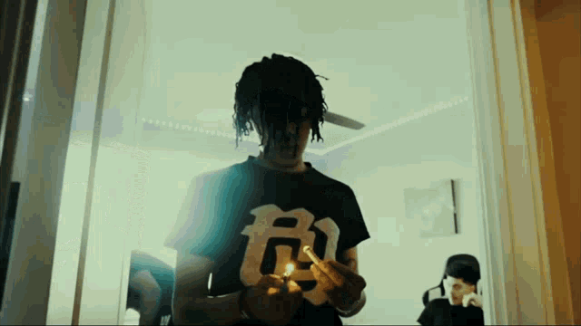 a man wearing a black shirt with the letter g on it lighting a cigarette