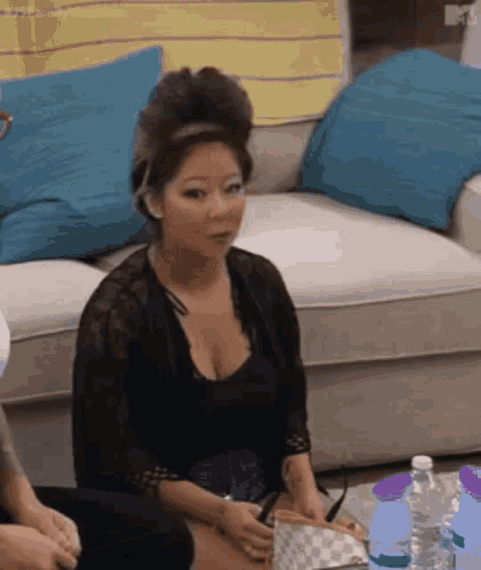 a woman in a black top is sitting on a couch with bottles of water .