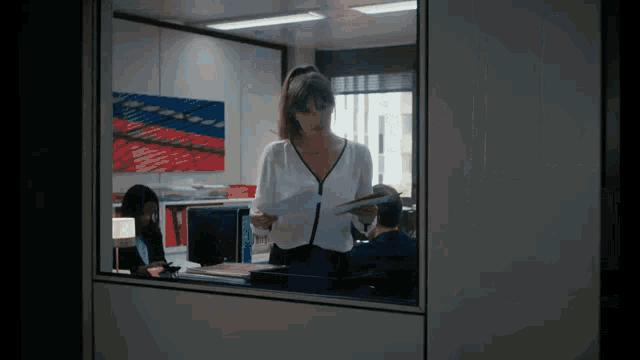 a woman standing in front of a window holding papers