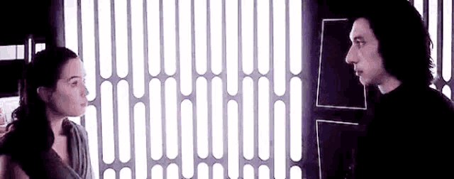 a man and a woman are standing next to each other in front of a window .