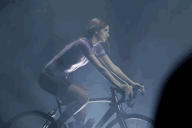 a woman in a purple shirt is riding a bike in a dark room