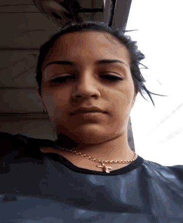 a woman wearing a cross necklace and a black shirt looks at the camera
