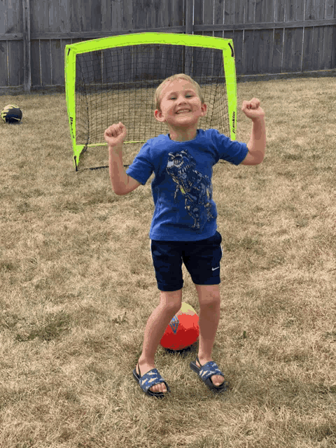a young boy in a blue shirt stands in front of a yellow goal