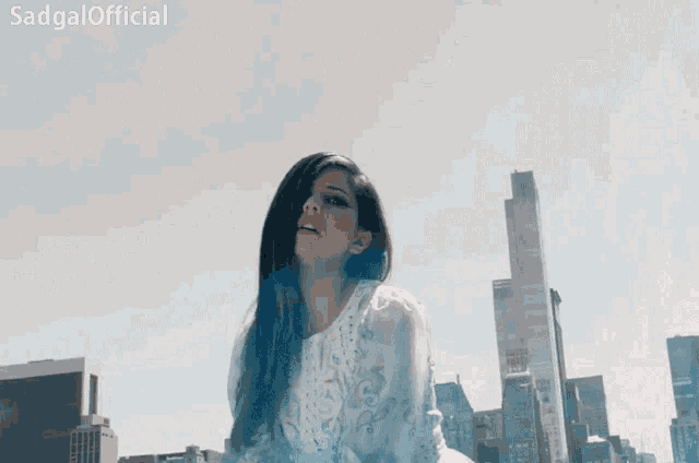 a woman in a white dress is standing in front of a city skyline with the words sadgal official written above her