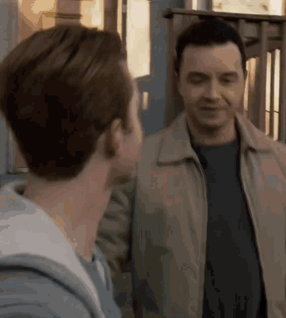 two men are standing next to each other and looking at each other . one of the men is wearing a jacket .