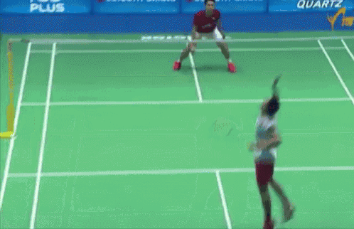 two men are playing badminton on a court with a banner that says quartz on it