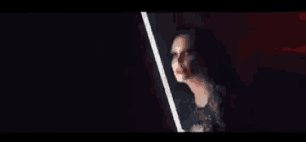 a woman is standing in front of a mirror in a dark room holding a light saber .