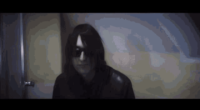 a man wearing sunglasses and a black jacket stands in a dark room