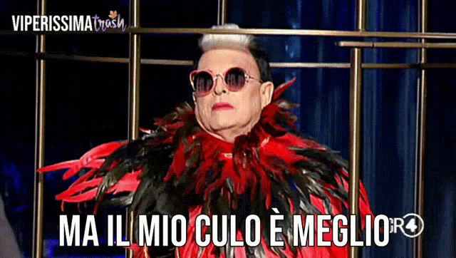 a man wearing sunglasses and a red and black feathered coat says " ma il mio culo e meglio "