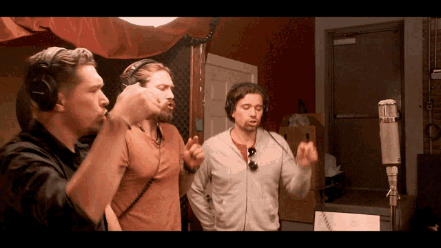three men wearing headphones singing into microphones in a room