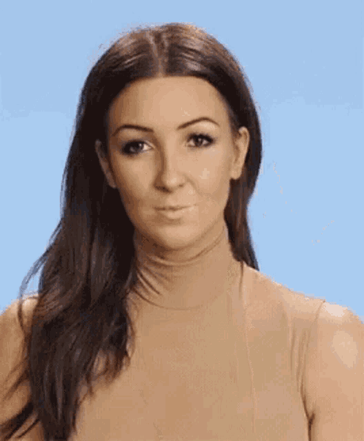 a woman wearing a tan turtleneck is making a funny face against a blue background .