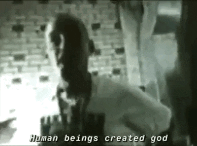 a black and white photo of a man standing next to a brick wall with the words `` human beings created god '' .