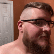 a man with glasses and a beard is looking at himself in the mirror .