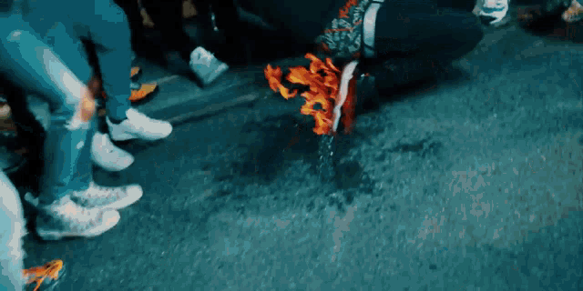 a group of people are standing around a person kneeling on the ground with a shoe on fire .
