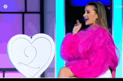 a woman in a pink top is sitting in front of a white heart with the number 2 on it