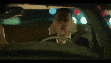 a man in a suit is driving a car and making a face