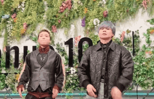 two men are dancing in front of a wall with flowers and the number 10