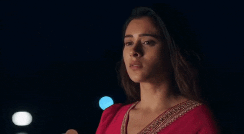 a woman in a red saree is standing in the dark looking at the camera .