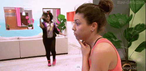 a woman in a pink tank top is looking at another woman in a living room ..
