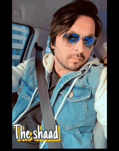 a man wearing sunglasses and a denim jacket is sitting in a car with the shaad written on the bottom