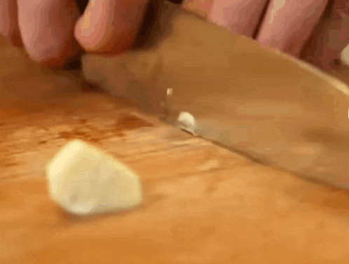 a person is cutting a piece of garlic with a knife on a cutting board .