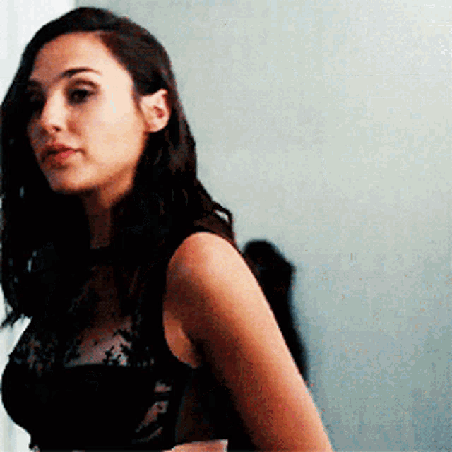 a woman in a black lace top is standing in front of a blue wall .