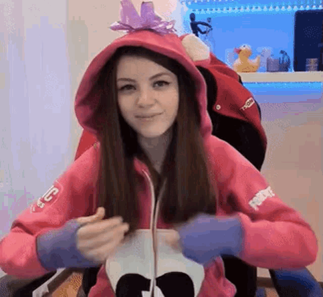 a girl wearing a pink hoodie and blue gloves is sitting in a chair and smiling .