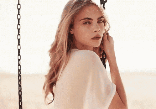 a woman in a white shirt is sitting on a swing on the beach .