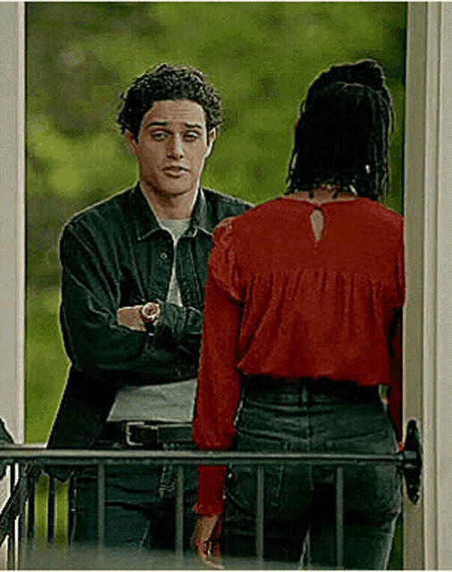 a man and a woman are standing next to each other on a balcony . the woman is wearing a red blouse .