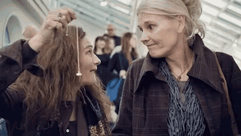 two women are standing next to each other and looking at each other . one woman is holding a pendulum in her hair .