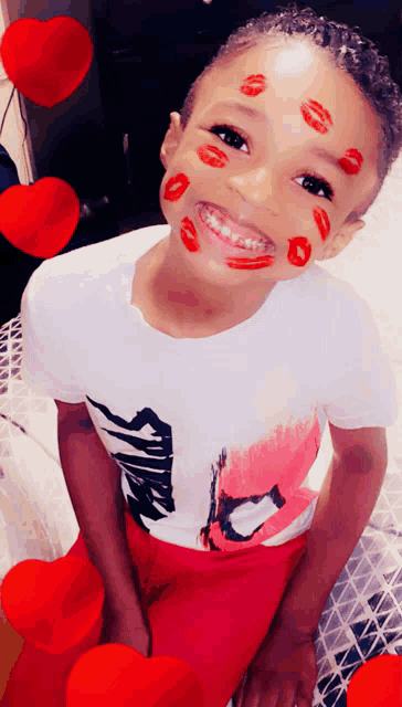 a young boy with red lipstick kisses on his face is wearing a shirt that says spider-man