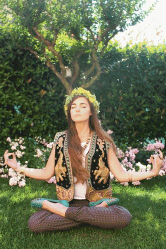 a woman with a flower crown on her head sits in a lotus position