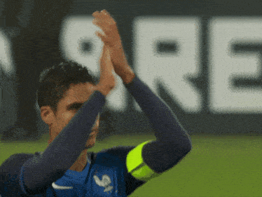 a soccer player applauds in front of a large sign that says ' re '