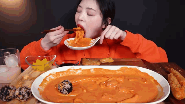 a woman in an orange sweater is eating a large plate of food