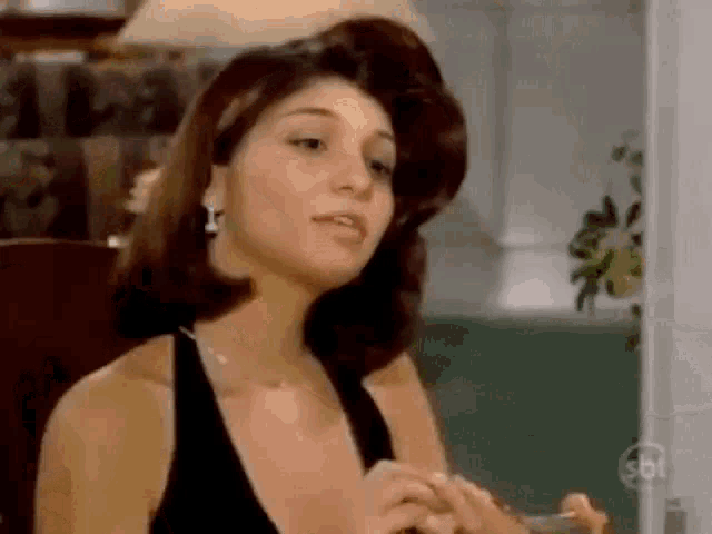 a woman in a black dress and earrings is sitting in a chair in a room .