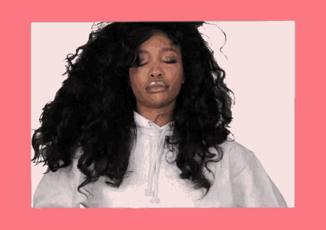a woman with curly hair is wearing a white hoodie and has her eyes closed