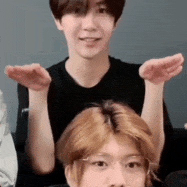 two young men are sitting next to each other on a couch with their hands in the air .